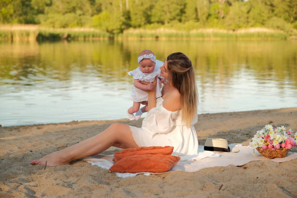 a beautiful girl in a white dress with a newborn baby is sitting on the beach, on the sand. a beautiful girl in a white dress with a newborn baby is sitting on the beach, on the sand. 3 months pregnant belly stock pictures, royalty-free photos & images
