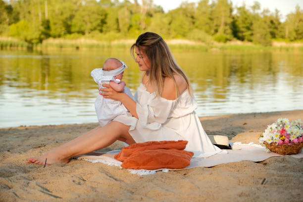 a beautiful girl in a white dress with a newborn baby is sitting on the beach, on the sand. a beautiful girl in a white dress with a newborn baby is sitting on the beach, on the sand. 3 months pregnant belly stock pictures, royalty-free photos & images