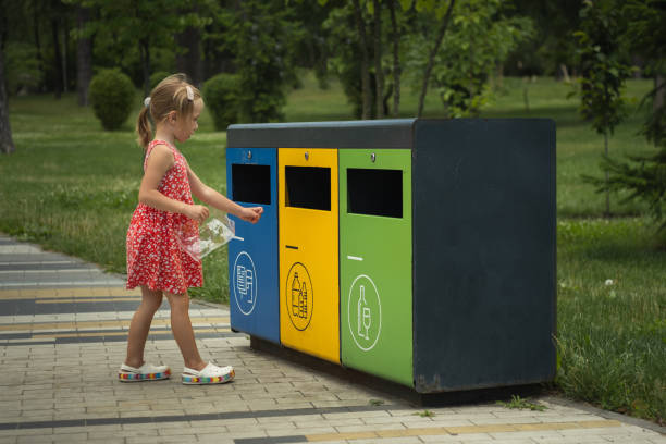 istock Cute little girl throw plastic garbage into yellow container in a park. Garbage sorting set. Bins with symbols for glass, paper and plastic trash. Care of environment by waste sorting 1412010358