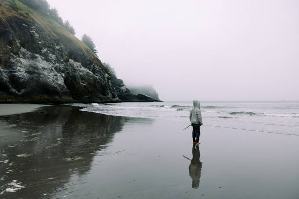 A Caucasian boy stands on the wet sandy beach, feeling the thrill of the Pacific Ocean as he looks at the view.  The beauty of the beach in the Pacific Northwest.  Shot at Waikiki Beach, Cape Disappointment, Washington state, USA.