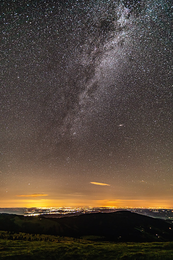astrophotography from high up of night sky over illuminated city with many stars, galaxy, far away planets and milky way