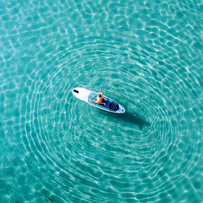 Mature man is training on a SUP board on the beach on a sunny morning.