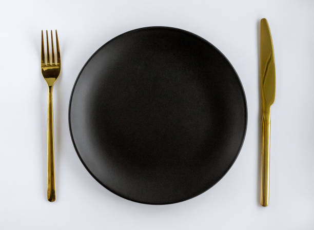 istock Black empty ceramic plate with golden cutlery on a white background. Center composition. 1412017255