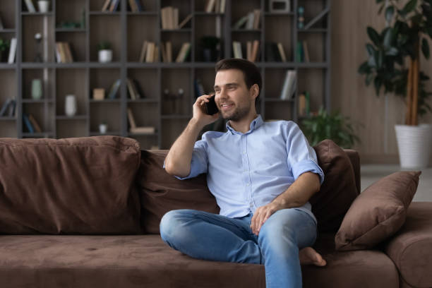 istock Smiling man chatting by phone call, relaxing on comfortable couch 1412021222