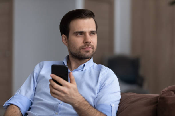 Head shot thoughtful man holding smartphone, looking in distance