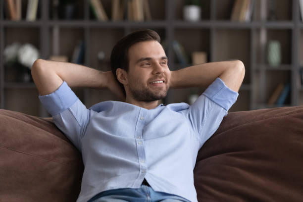 istock Smiling dreamy man relaxing, stretching on couch at home 1412021252
