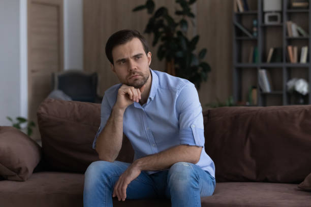 istock Thoughtful upset man looking in distance, sitting on couch alone 1412021256