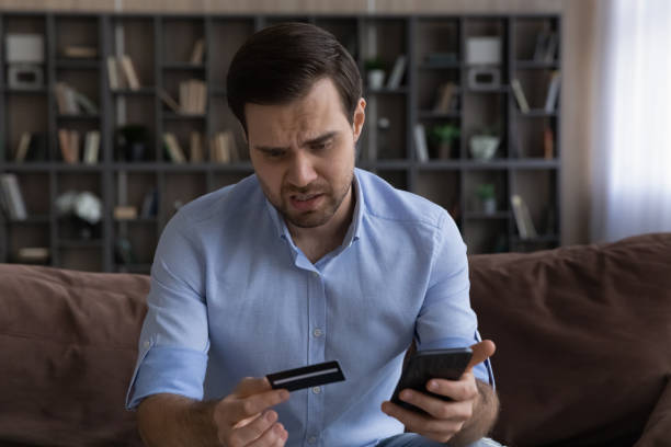 istock Unhappy man having problem with credit card, holding smartphone 1412021259