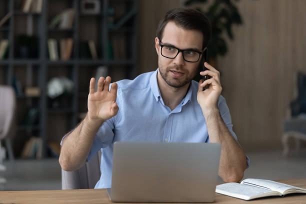 istock Confident serious businessman in glasses talking on phone, using laptop 1412021358