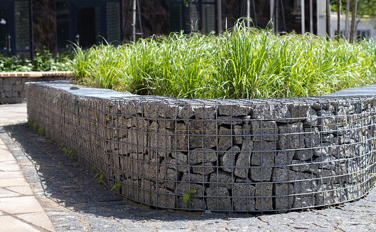 Basket support wall made of granite gabion. Gabions in the garden. Modern Gabion fence with stones in wire mesh. Gabion wire mesh fencing with natural stone and shrubs