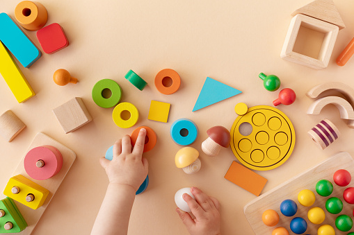 Toddler activity for motor and sensory development concept. Baby hands with colorful wooden toys on table from above.