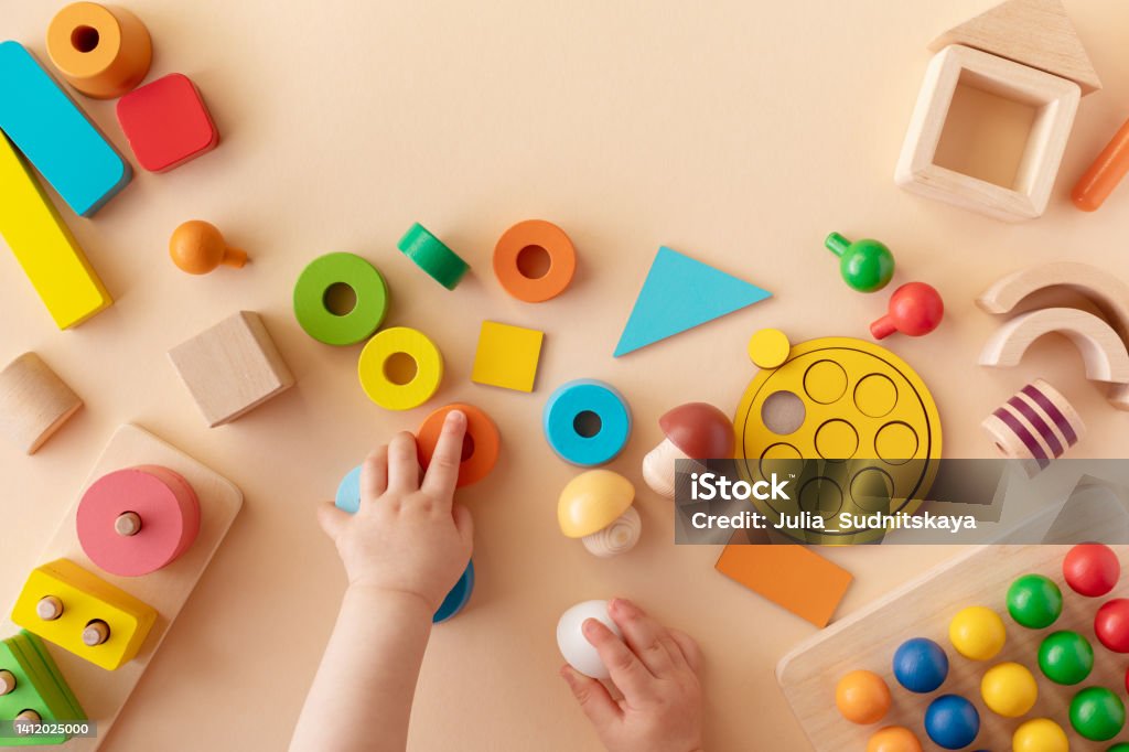 Toddler activity for motor and sensory development. Baby hands with colorful wooden toys on table from above. Toddler activity for motor and sensory development concept. Baby hands with colorful wooden toys on table from above. Toy Stock Photo