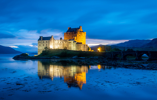 Dornie, Scotland, UK, July 19, 2022.  Eilean Donan Castle illuminated in the evening with beautiful lights and reflection in the water.