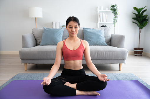 Beautiful happy girl practicing yoga in lotus position in livingroom