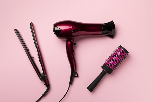Hair dryer, straightener and brush on color background, top view.