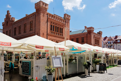 Kolobrzeg, Poland - June 23, 2016: Temporary cafes and restaurants covered with a square umbrellas open for the summer season and behind them the Town Hall building built of red brick can by seen
