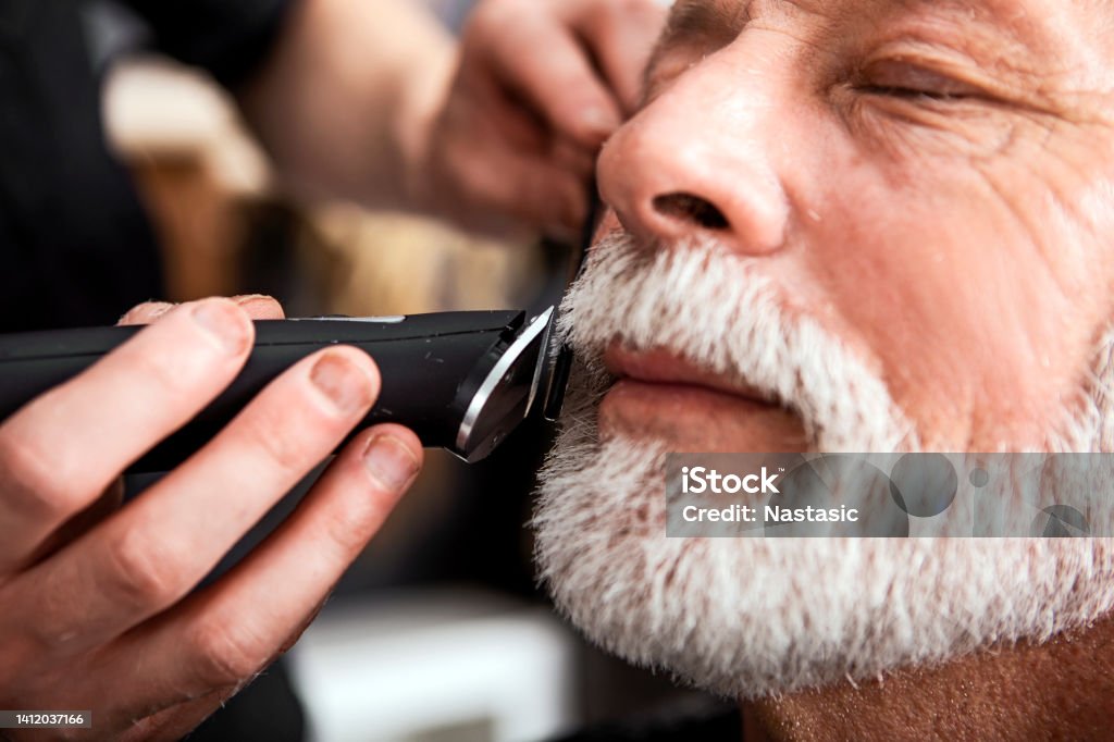 Senior man in barber shop Man getting haircut in barber shop Barbers Pole Stock Photo
