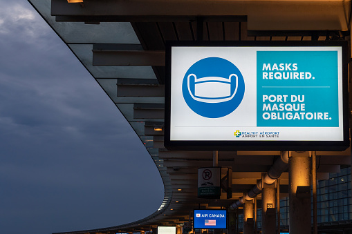 Mississauga, Ontario, Canada - July 5, 2022: Masks Required warning sign at passenger drop-offs curbside in Toronto Pearson International airport in early morning, Mississauga, Ontario, Canada.
