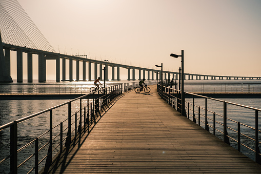 Lisboa , Portugal; 31 July 2022: Cyclists riding along the Tagus Footbridge in Lisbon at sunrise