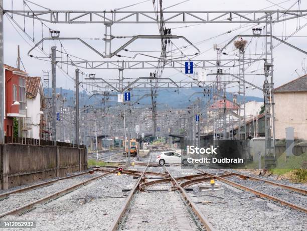 White Car Crossing A Level Crossing Over The Train Tracks At The Entrance Of The Monforte De Lemos Station Under The Catenary Cables And The Station In The Background Stock Photo - Download Image Now