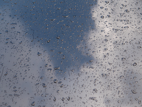 Water drops on the hood of a metallic black car and the reflection of clouds and sky after a storm