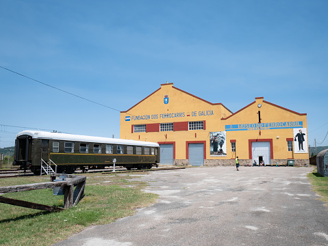 Monforte de Lemos, Lugo, Spain; 07-23-22: Main facade of the buildings of the foundation of the Galician railways and the railway museum, a green wagon outside and the little tourist train in motion