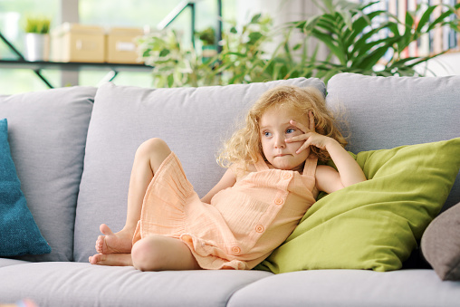 Cute lovely girl resting on the couch at home, she is thinking and looking away