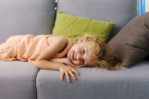 Cute lovely girl resting on the couch at home, she is lying down and smiling at camera