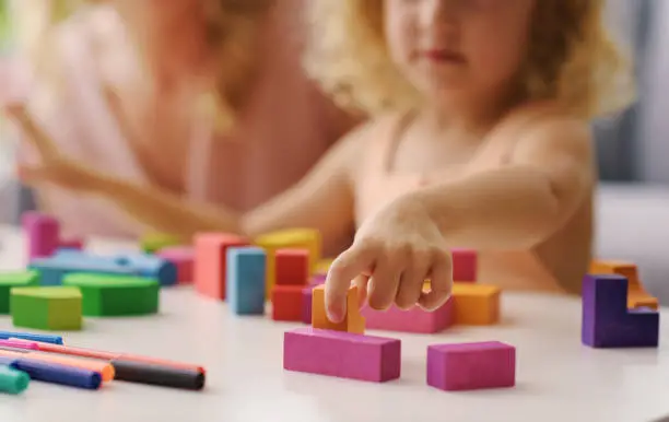 Child playing with wooden blocks, her mother is next to her, hand close up
