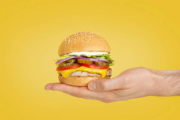 istock hamburger in hand on yellow isolated background 1412061147