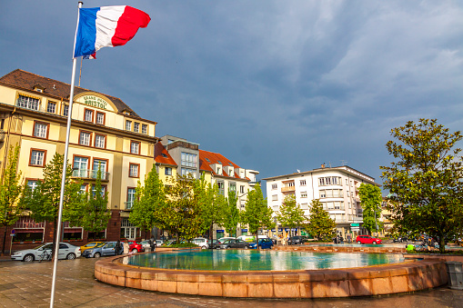 Colmar, France - May 2, 2019: Railway station square (Place de la Gare) in Colmar city, Alcase, France. Square has a beautiful fountain divided into two parts. Grand Hotel Bristol on background