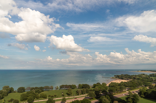 A beautiful panoramic view of Lake Michigan with fluffy cumulus clouds in a bright blue sky reflecting off the calm water as people enjoy the beach below on a warm summer afternoon.