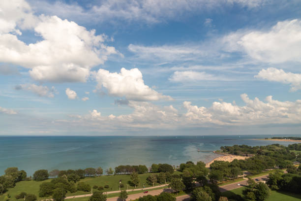 A beautiful panoramic view of Lake Michigan with fluffy cumulus clouds in a bright blue sky reflecting off the calm water as people enjoy the beach below on a warm summer afternoon. stock photo
