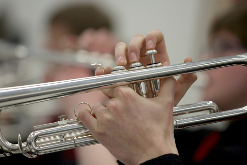 A closeup of the hands of a musician playing a trumpet