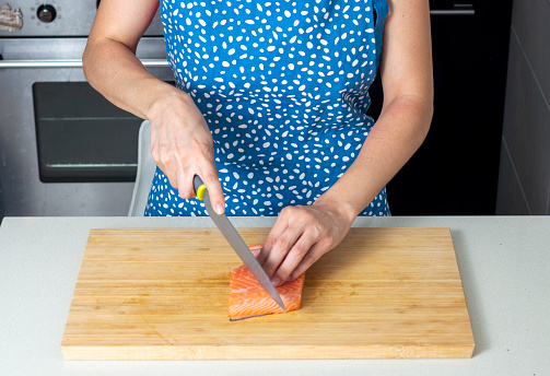 Woman cutting fresh salmon fillet on wooden plank