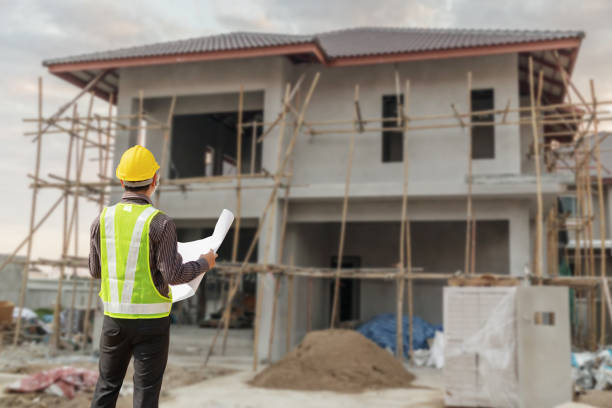 young professional engineer in protective helmet and blueprints paper at the house building construction site