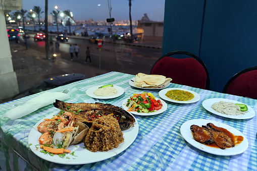 Various seafood dishes on the table in the restaurant against the backdrop of a beautiful view of night city and the sea.
