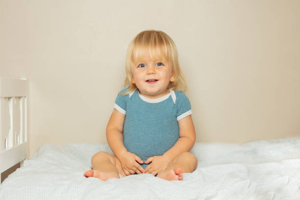 istock Smiling blond toddler boy sit on the bed in nursery 1412089538