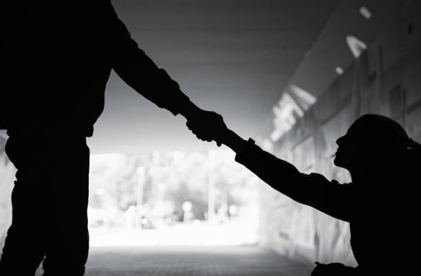 Man giving a helping hand to woman in need sitting on dark street. Kindness, love concept. beggar stock pictures, royalty-free photos & images