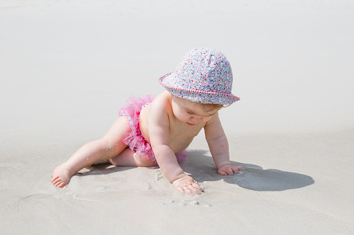 Adorable little girl is playing with sand at beach near to sea. Sensory development for kids outdoors.
