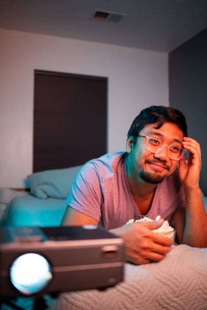 istock (Cringing) Man Watching a Movie in Bed with Projector 1412119720