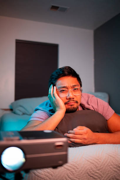 istock (Thinking) Man Watching a Movie in Bed with Projector 1412120382
