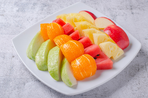 Fresh fruit party on white plate. Beautifully cut apples, oranges, pineapples and guavas.