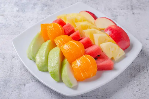 Photo of Fresh fruit party on white plate. Beautifully cut apples, oranges, pineapples and guavas.