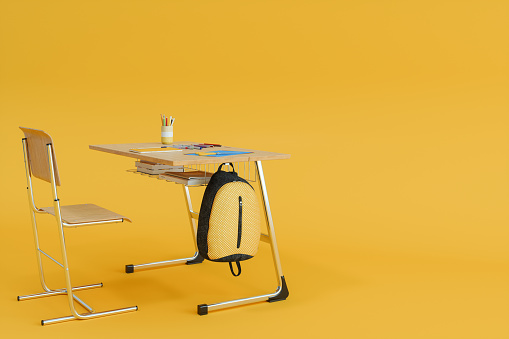 Back To School. Wooden School Desk With School Supplies And Backpack On Yellow Background
