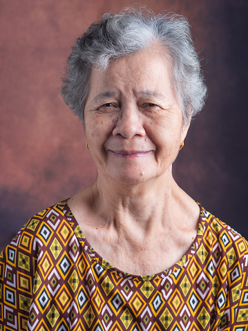 Portrait of beautiful senior woman with white hair smiling and looking at camera while standing with vintage background. Concept of old people and healthcare