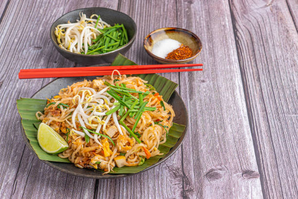 パッドタイは、木製のテーブルの上に黒い皿の上にバナナの葉の上に野菜とレモンスライスを添えて提供。タイ料理は有名です。テキスト用のスペースがあるトップビュー。タイの伝統食の� - pad thai ストックフォトと画像
