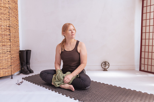 A middle aged woman practices yoga in a clean white urban studio wearing regular gym clothes.