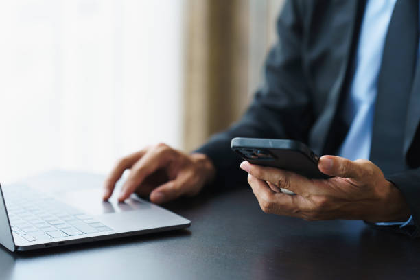 Close up businessman using a smartphone and a laptop while working from home. Close up businessman using a smartphone and a laptop while working from home. smart phone telephone research tax stock pictures, royalty-free photos & images