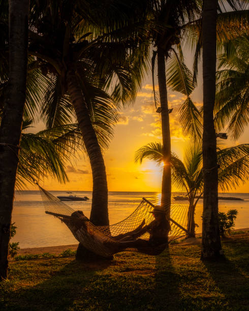 a couple of men and women watching the sunset on a tropical beach in a hammock in Mauritius with palm trees by the Tropical sunset on the beach in Mauritius.